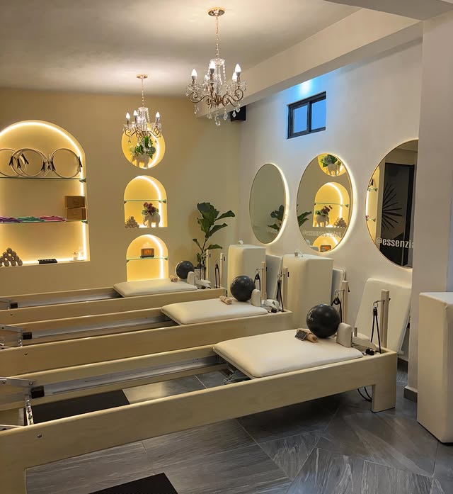 Interior del estudio Essenzia Pilates, con camas reformer de madera clara, espejos circulares y luz cálida.