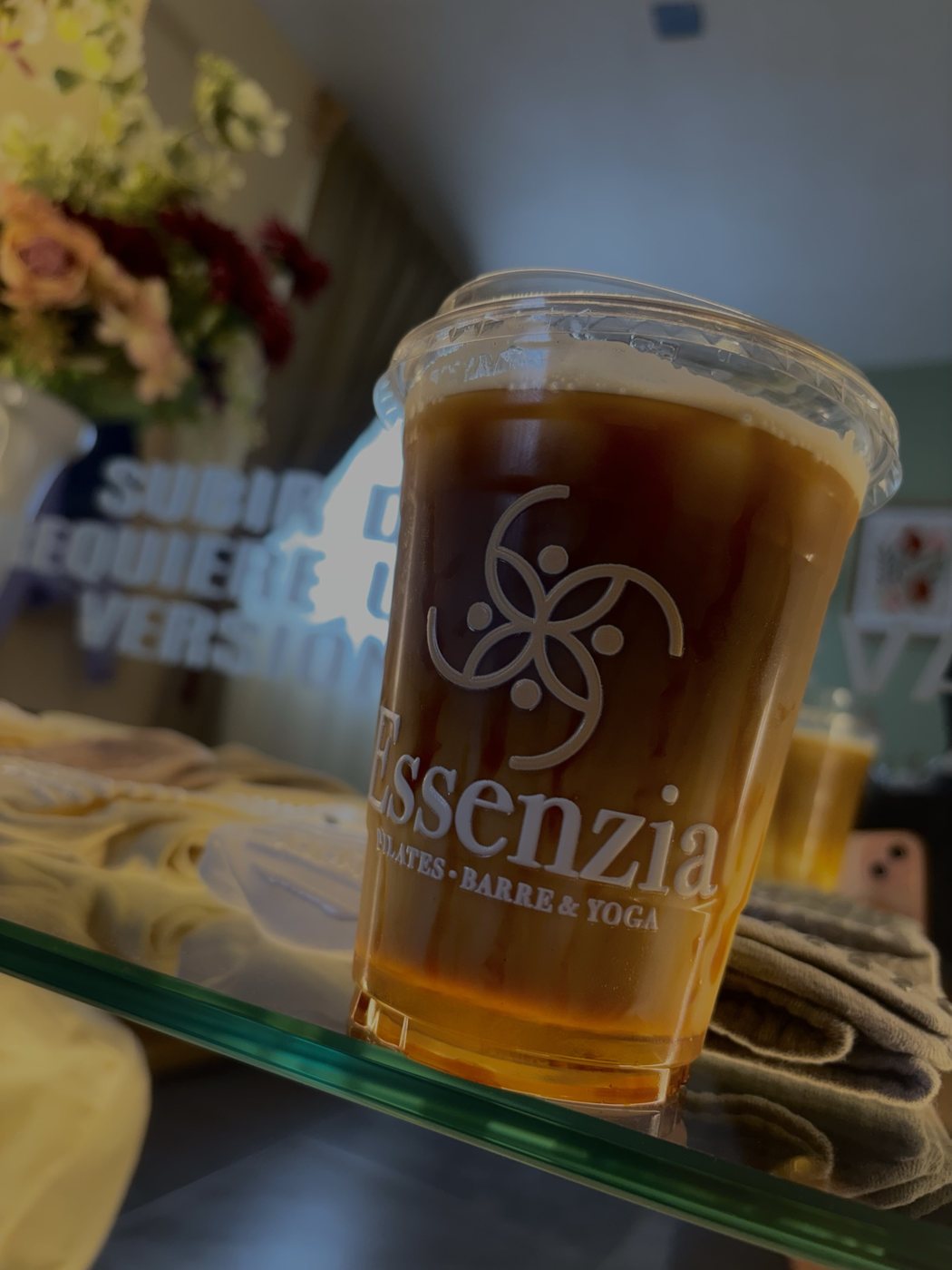 Vaso de bebida con el logotipo de Essenzia, un emblema floral sobre el nombre del estudio.
